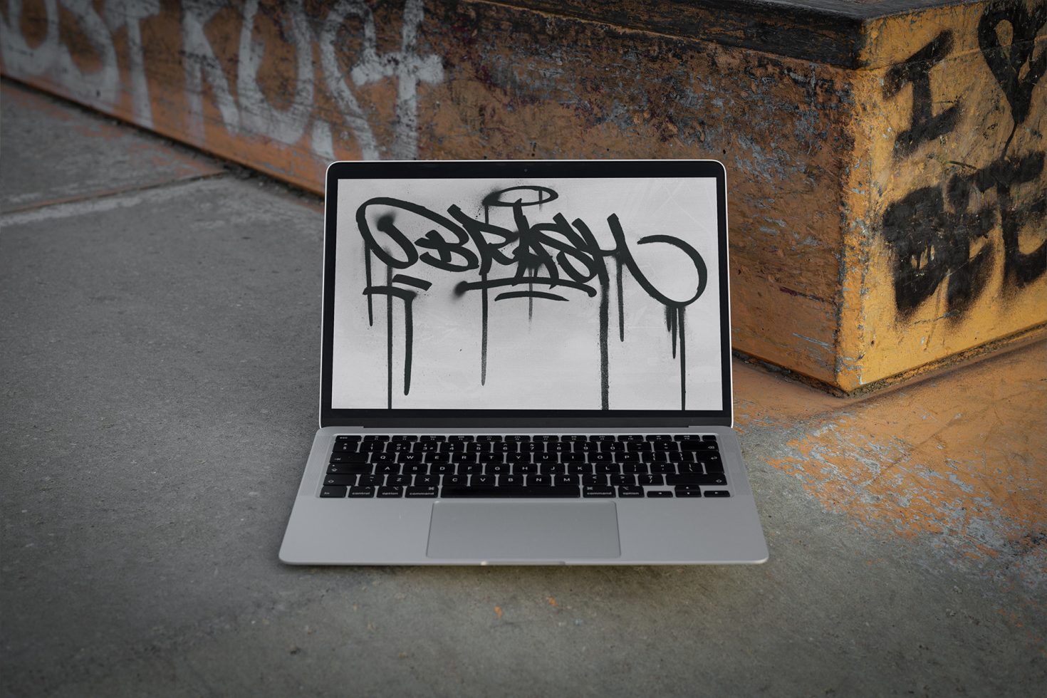 Laptop on urban ground displaying graffiti-style font, ideal for designers looking for edgy typography inspiration in mockups and graphics.